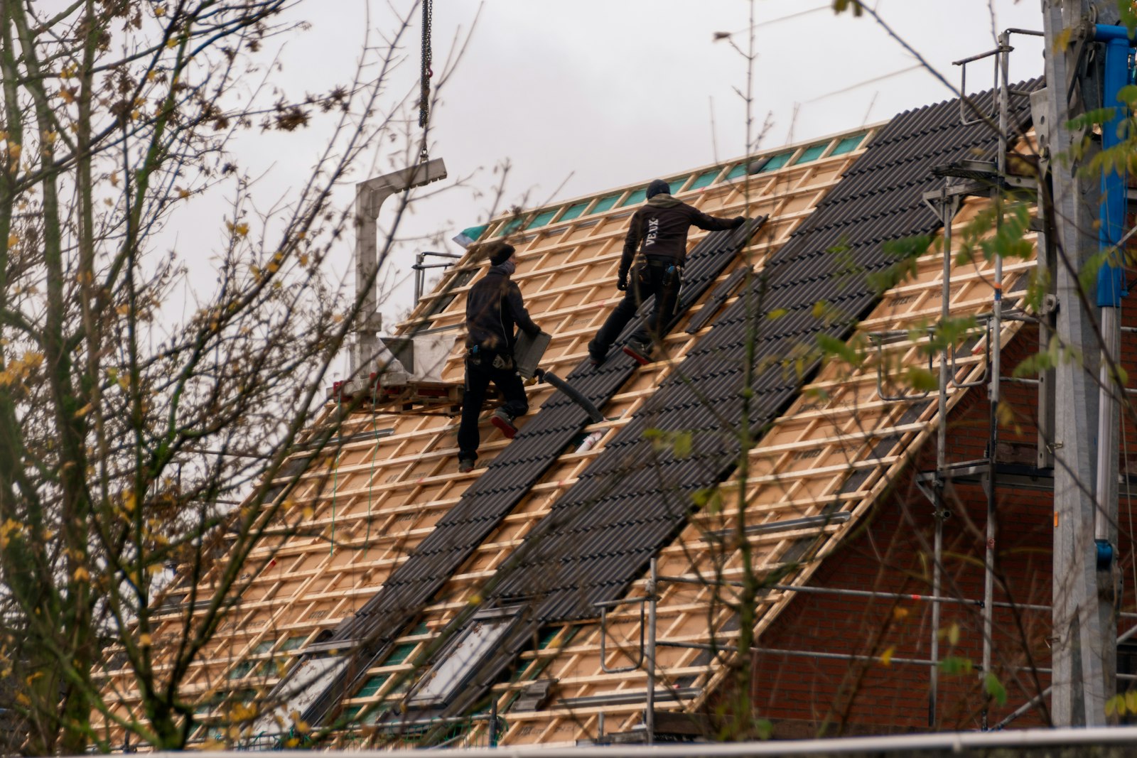 Two roofers working on a steep residential roof mid-renovation, laying new roofing over wooden battens